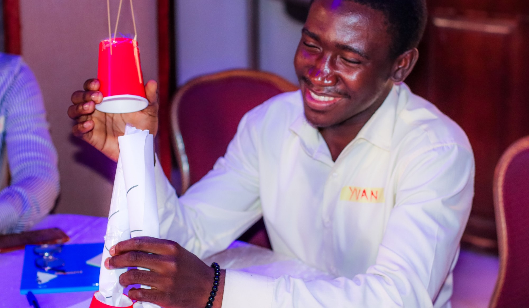 Un participant souriant construit une tour en papier et en gobelets lors d’un défi d’équipe pratique
