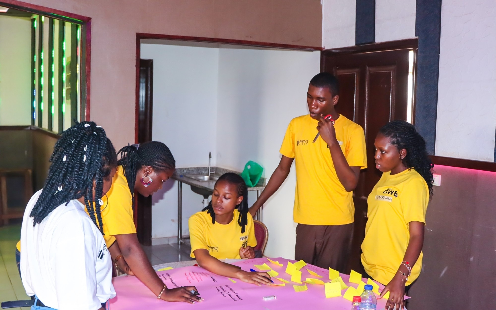 Fellows in yellow t-shirts planning together around a table covered in sticky notes