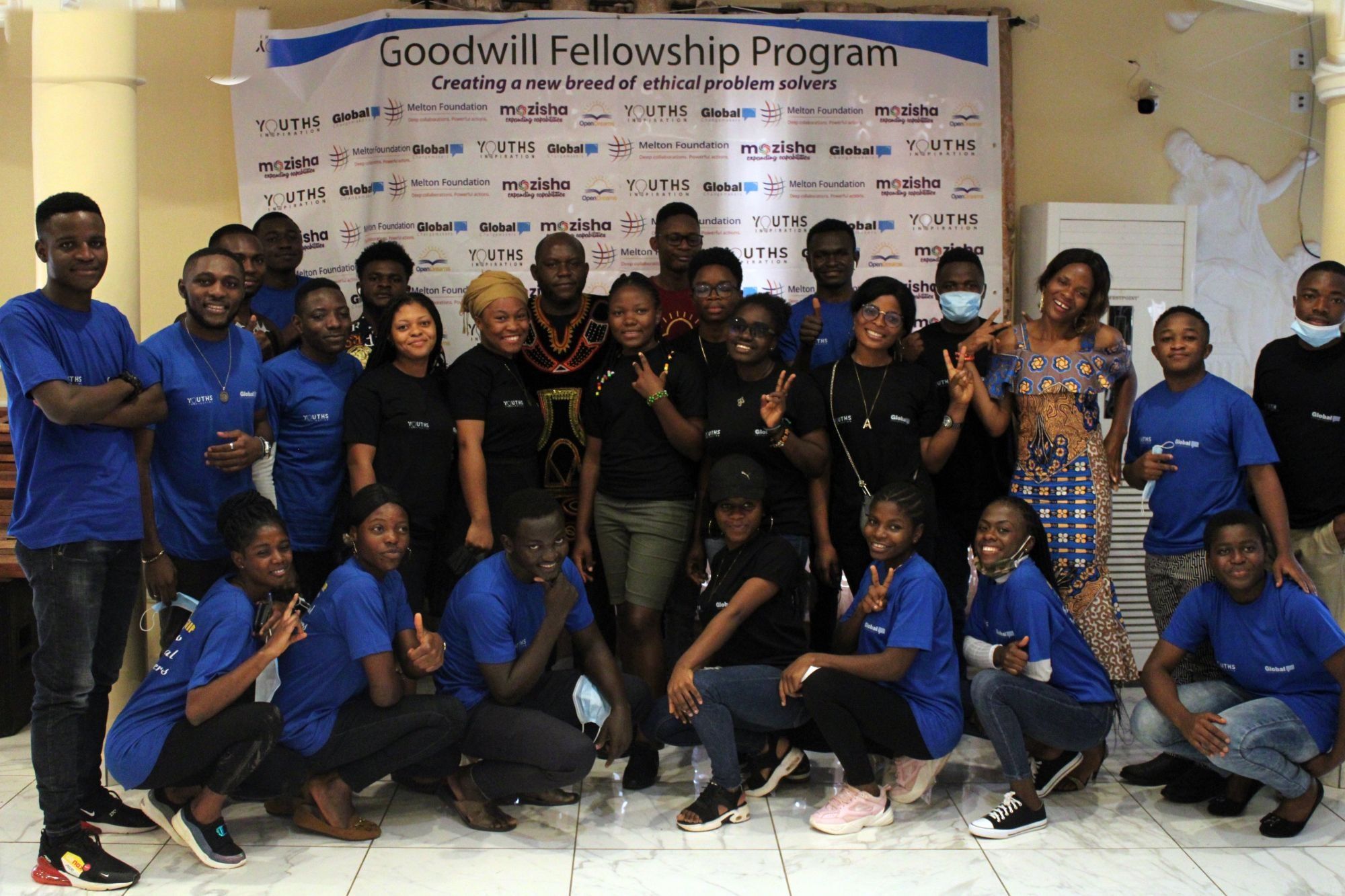 The first Goodwill Fellowship cohort in blue and black t-shirts in front of the programme banner