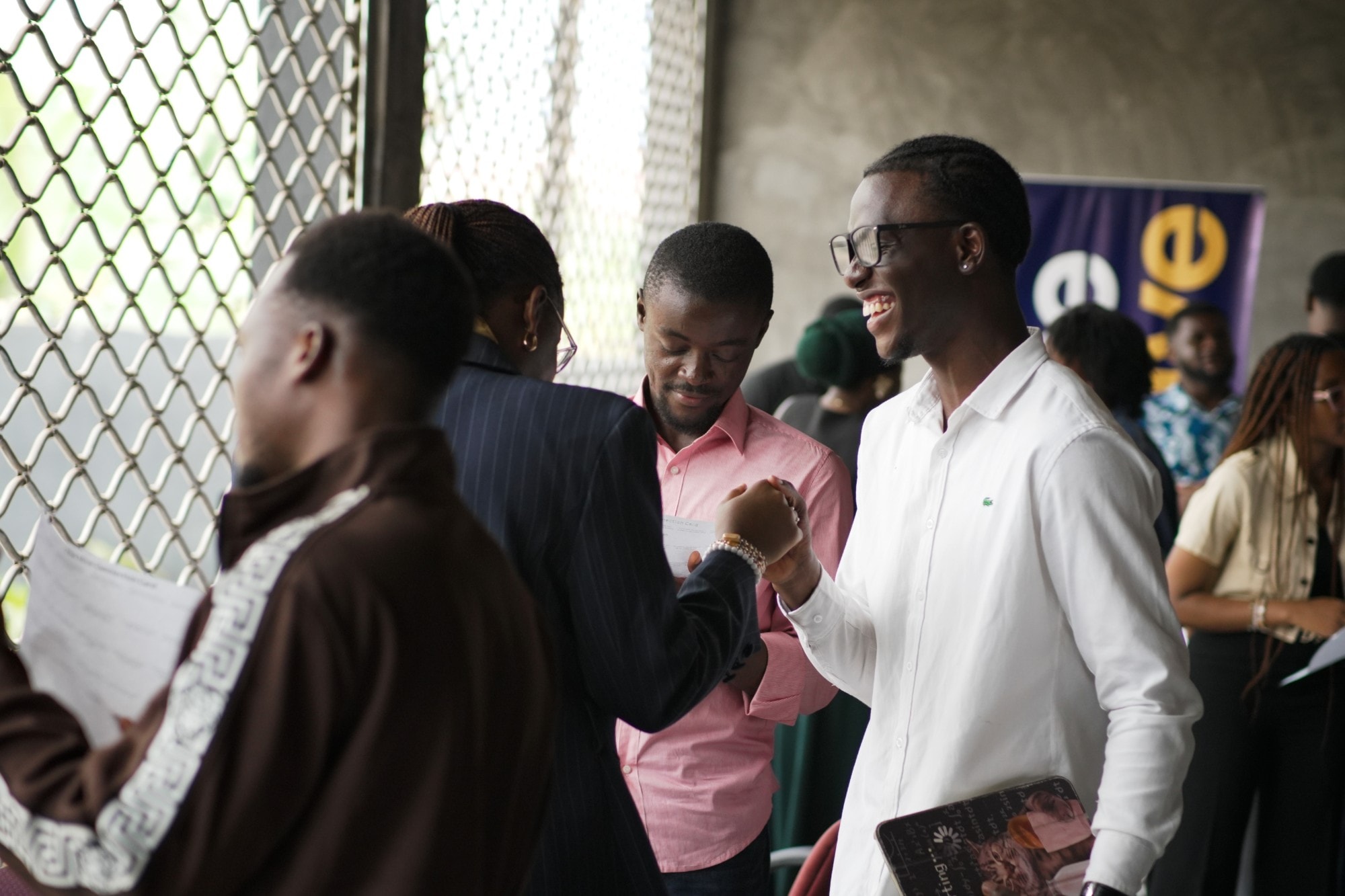 Un jeune homme souriant, en chemise blanche, échange un check avec une autre participante lors d’un événement de networking animé
