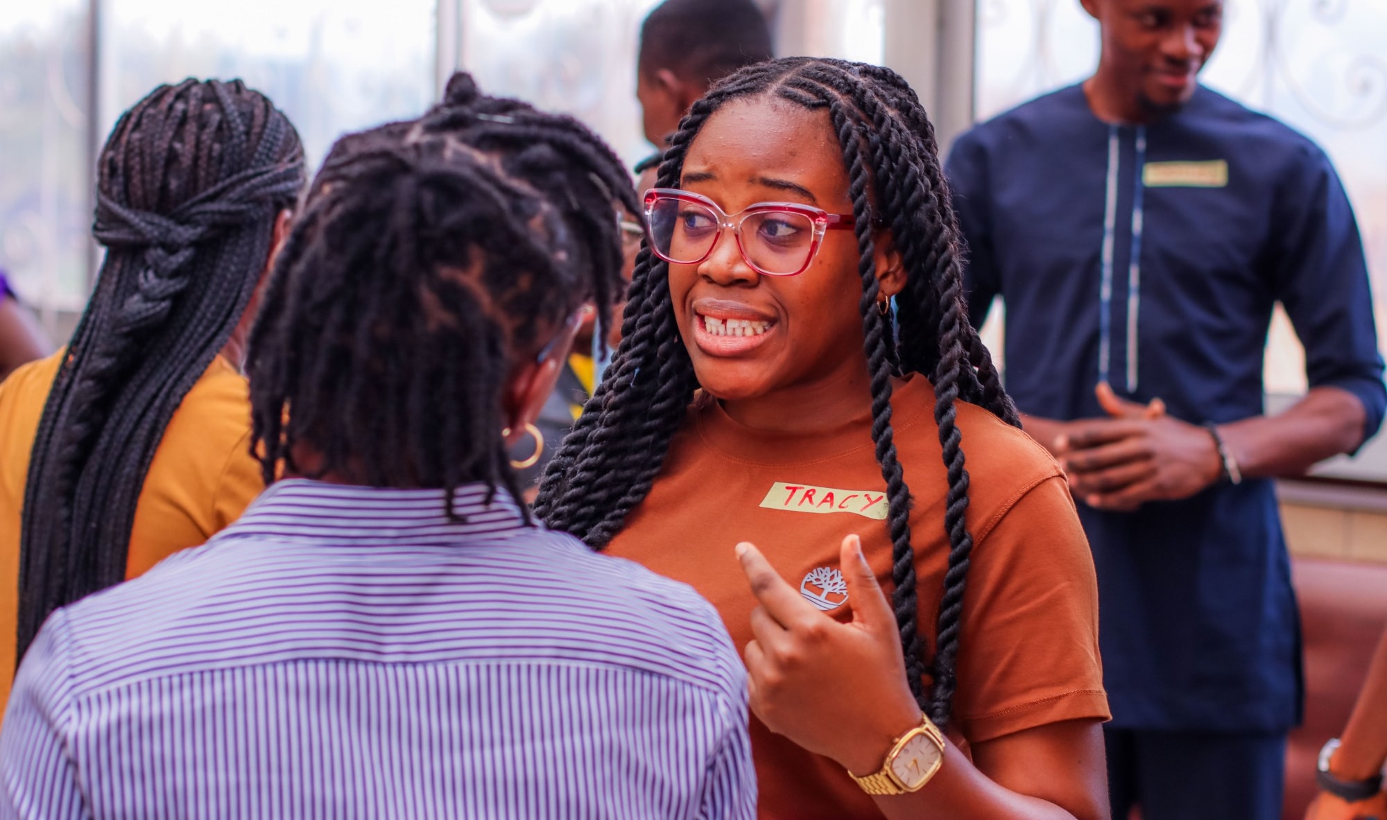 Une jeune femme aux lunettes rouges, portant un badge à son nom, explique un point à une camarade lors d’une session Impact Axis